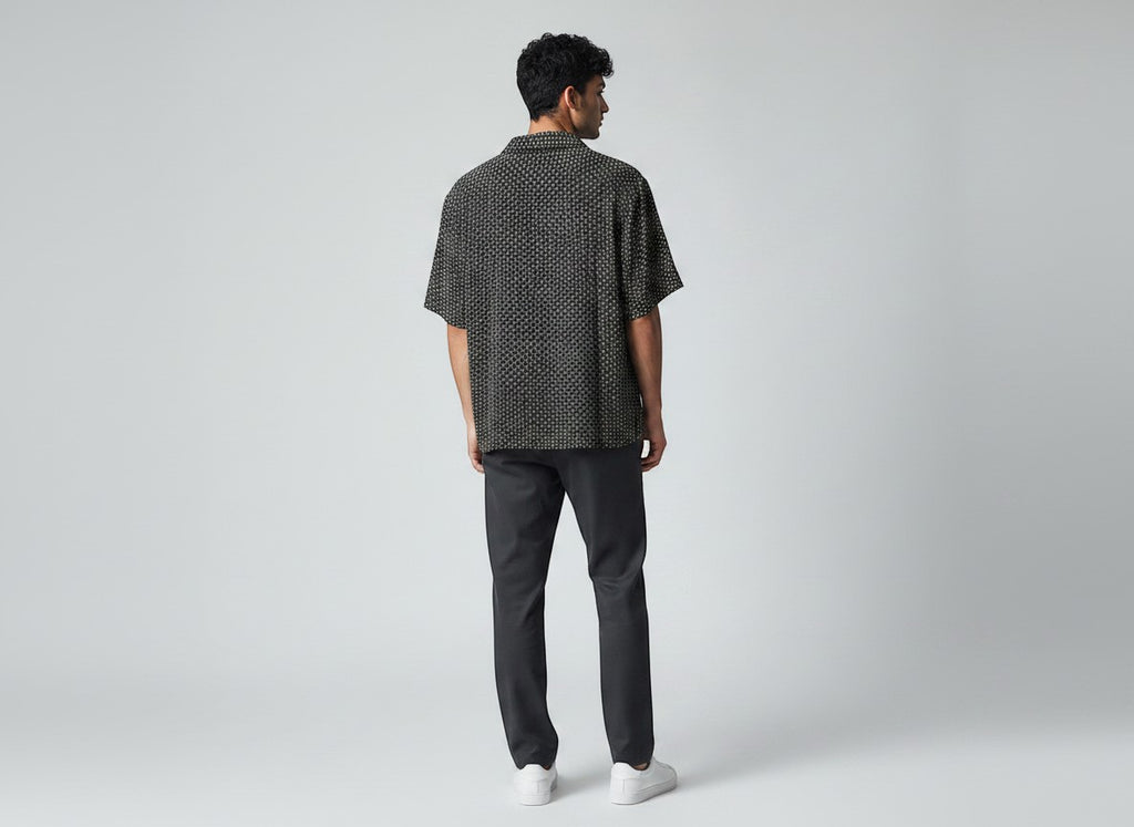 Man wearing an Anchor & Crew black short-sleeve button-down shirt with a white geometric pattern and dark trousers.